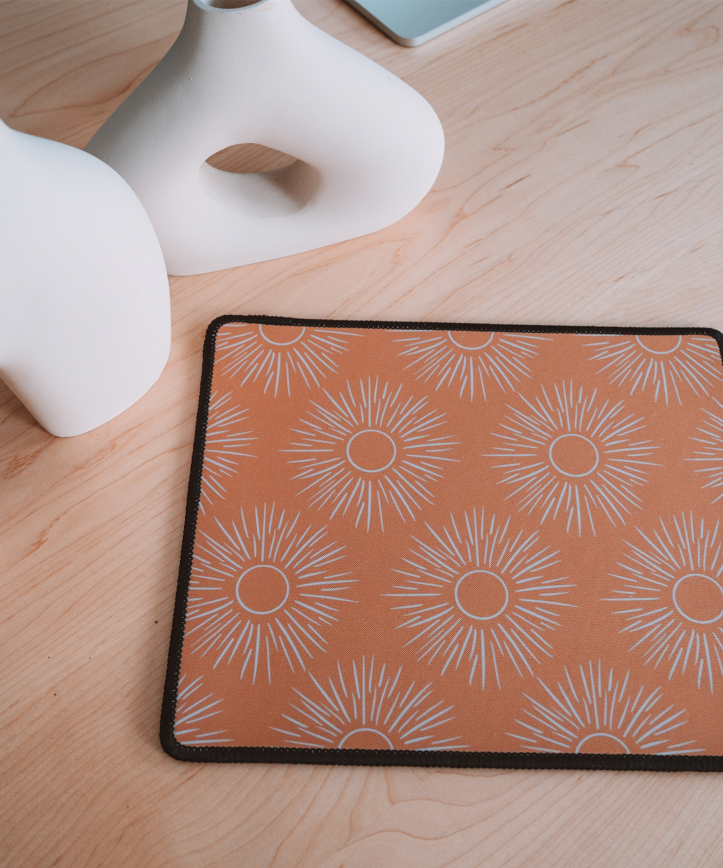 The Soleil mousepad is laying on a desk with two asymmetrical vases in the background
