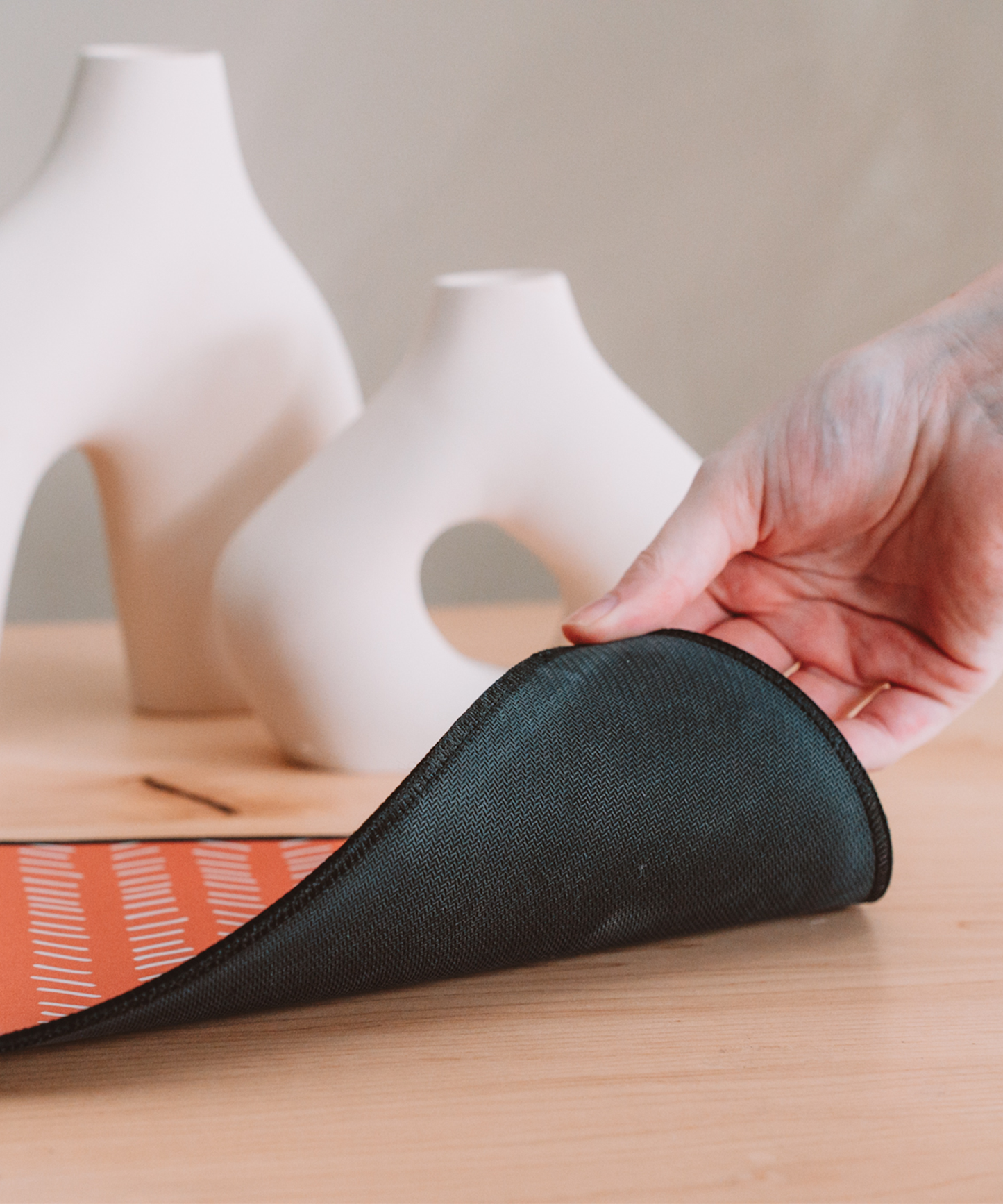 A hand is pulling up the corner of the Harrow mousepad to reveal the black anti-slip rubber backing