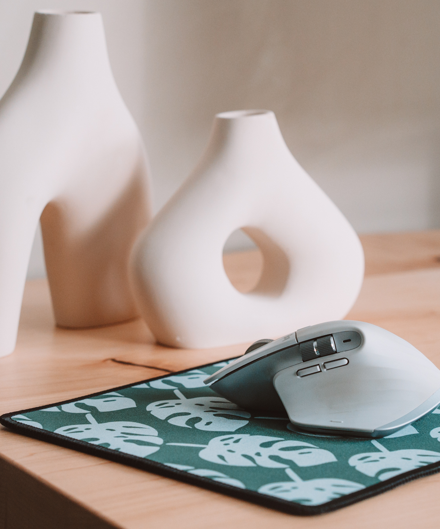 A mouse is sitting on top of the Monstera mousepad with two asymmetrical vases in the background