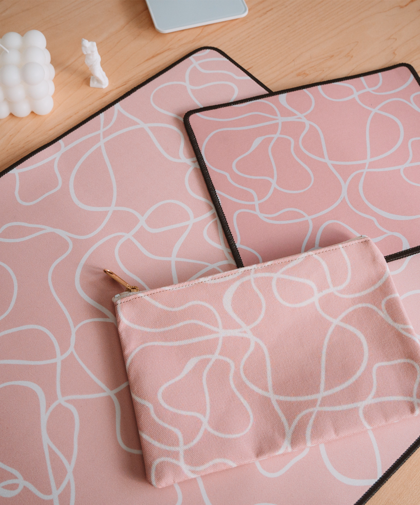 The Terrain mousepad is laying on a desk alongside the matching Terrain accessory pouch and Terrain desk mat. In the background is a bubble candle and a 3D printed mini statue.