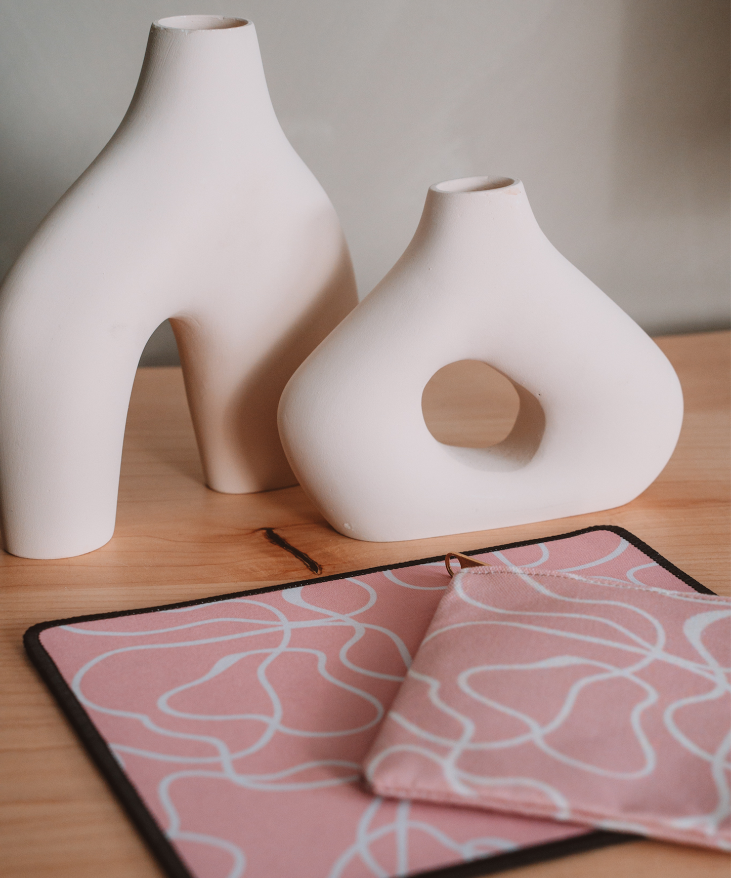 The Terrain mousepad is laying on a desk with the matching Terrain accessory pouch. In the background are two asymmetrical vases.