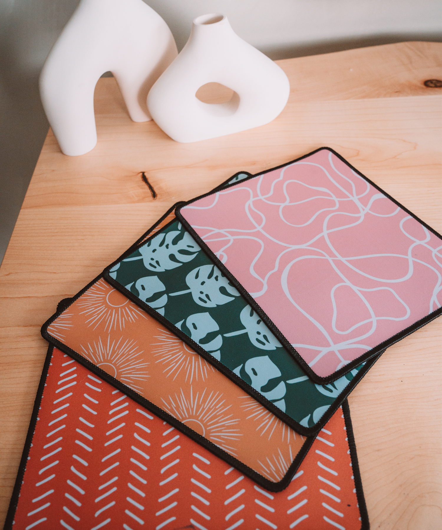 All mousepads are laying on a desk with two asymmetrical vases in the background. In order: Terrain, Monstera, Soleil, and Harrow.