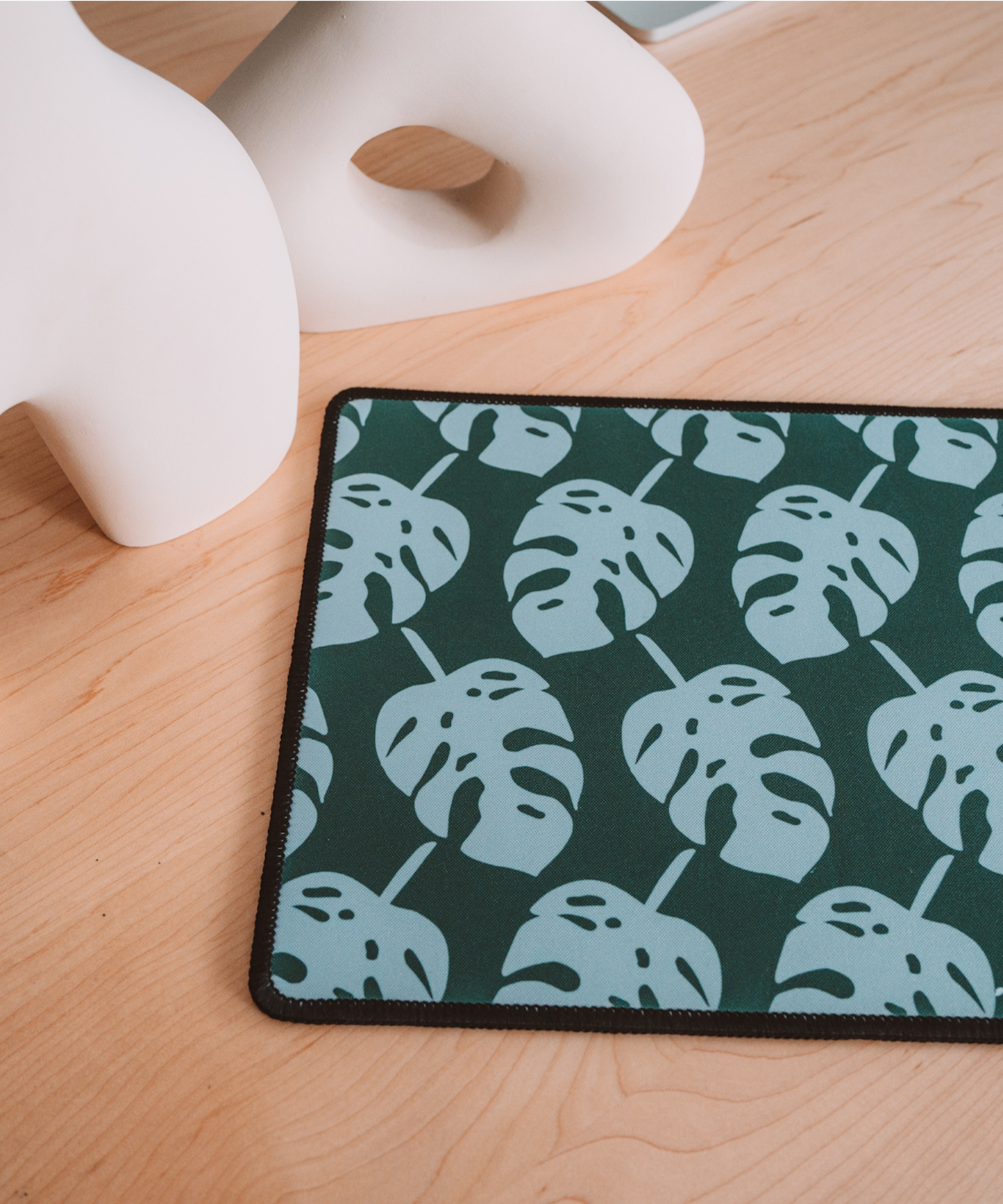 The Monstera mousepad is laying on a desk with two asymmetrical vases in the background