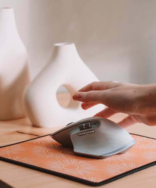 A hand is reaching for a mouse on top of the Soleil mousepad. In the background are two asymmetrical vases.