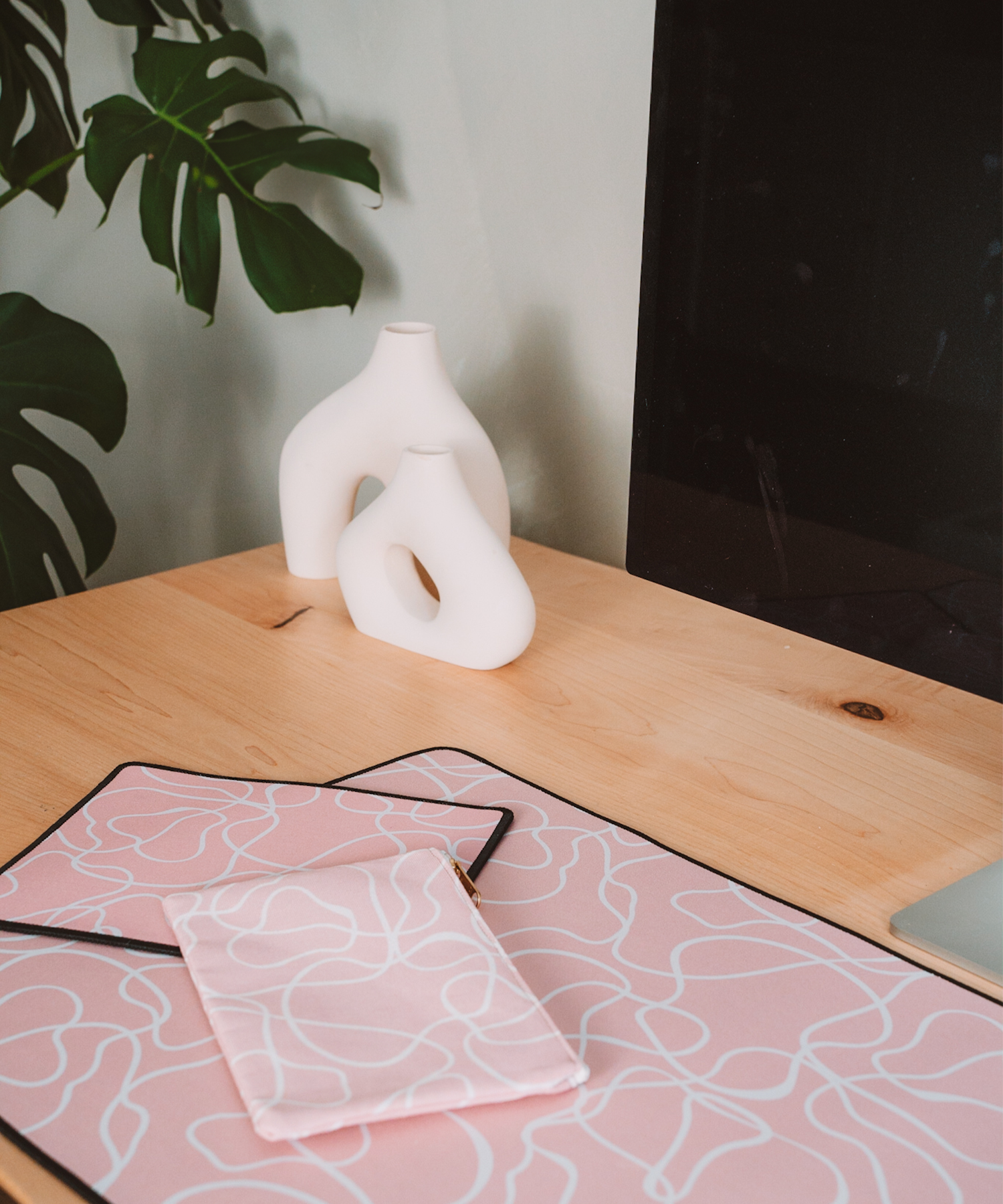 The Terrain mousepad, Terrain accessory pouch, and Terrain desk mat are sitting on a desk with the Apple Studio Display and two asymmetrical vases. In the distance, there is a monstera plant.